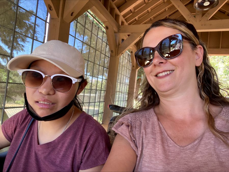 Photo of a woman and a child wearing sunglasses and smiling. There is a wood building like in the background.