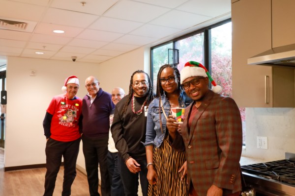 Tripplett + Ewell Family and Associates: Group of people smiling together indoors, some wearing Santa hats, during a festive RMHC holiday celebration.